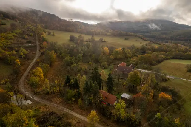 Aerial of an autumn valley with farmhouses, winding lanes and forest under drifting mist