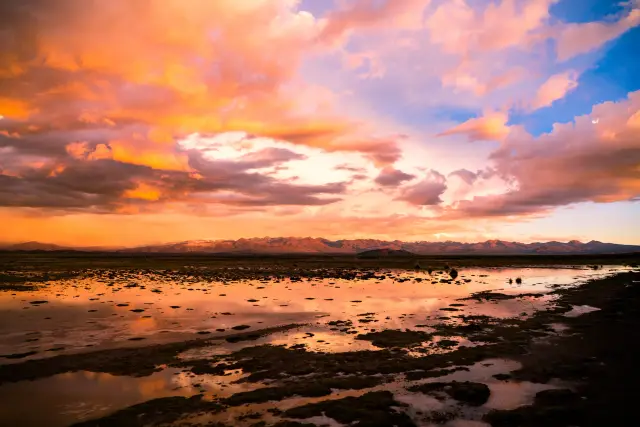 A vivid sunset and mountains reflected in marshy highland wetlands