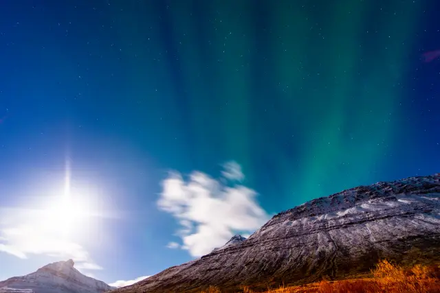 Green northern lights and a bright moon above snow-dusted mountains, Iceland