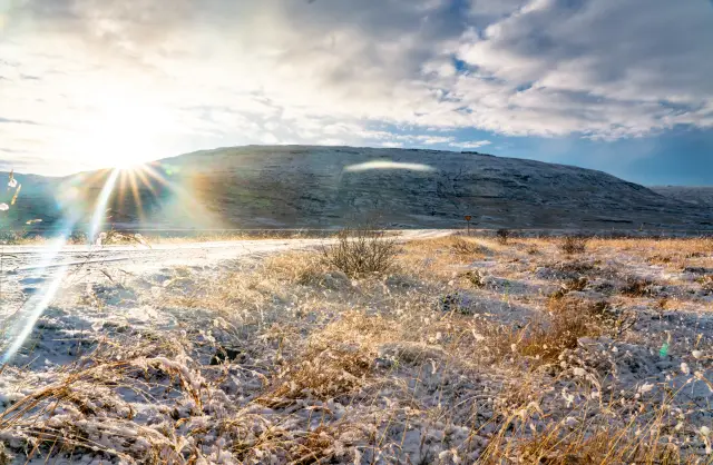 A bright sunburst over a frosty grassy plain below a snow-dusted mountain, Iceland