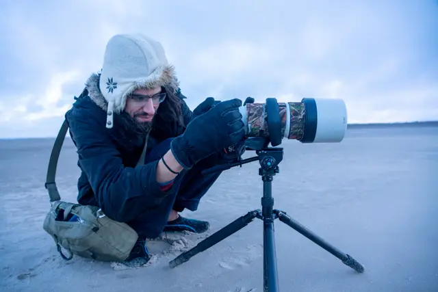 The photographer lying in the snow behind a tripod-mounted camera.